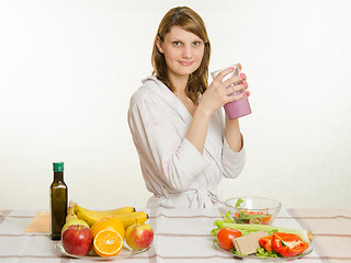 Image showing Young girl sitting at the kitchen table with a fruit milkshake in hand