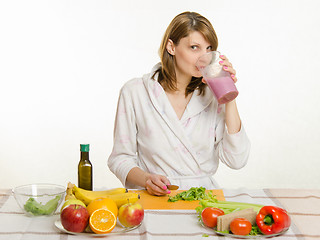 Image showing Young girl sitting at the kitchen table, drinking a fruit milkshake from a large cup