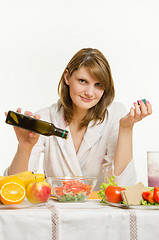 Image showing Young woman pouring oil into a vegetarian vegetable salad