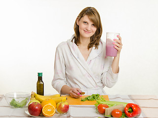 Image showing Young girl sitting at the kitchen table and holds a big glass of cocktail