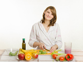 Image showing Happy housewife sitting at the table and cut the celery salad