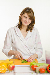 Image showing Housewife sitting at the table and cuts the greens for salad