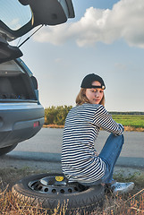 Image showing Young sad woman sits on spare wheel