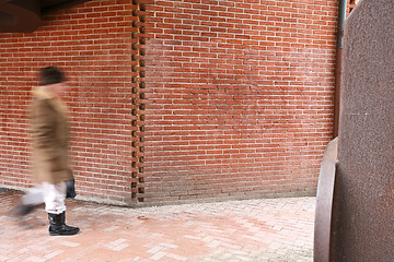 Image showing People passing by a brick wall