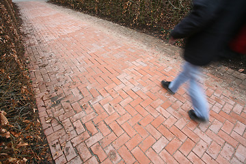 Image showing People passing by a brick wall