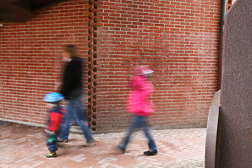 Image showing People passing by a brick wall