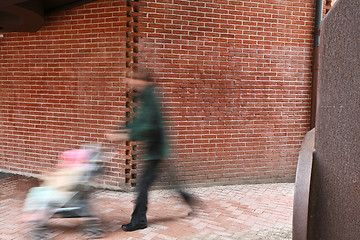 Image showing People passing by a brick wall