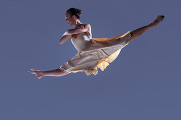 Image showing Young beautiful dancer in beige dress jumping on gray background