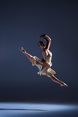 Image showing Young beautiful dancer in beige dress jumping on gray background