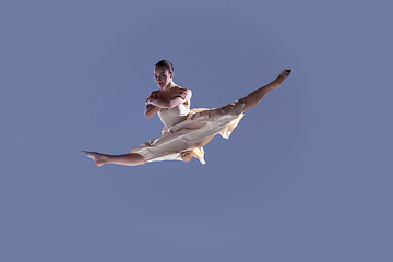 Image showing Young beautiful dancer in beige dress jumping on gray background