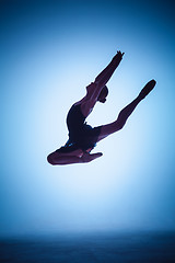 Image showing The silhouette of young ballet dancer jumping on a blue background.