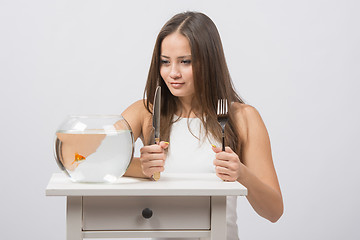 Image showing Girl holding knife and fork in hand and with an appetite for looking at the little goldfish