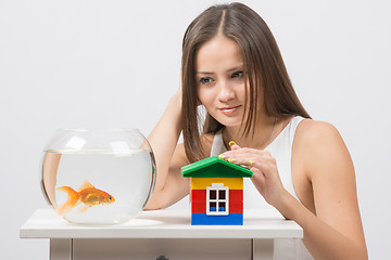 Image showing The girl looks at a goldfish and put her hand on the toy house