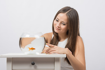 Image showing She knocks on the finger on the glass aquarium with goldfish