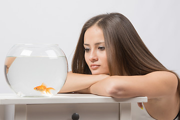 Image showing Sad young girl looking with indifference at the little goldfish