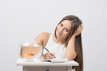 Image showing Girl writing in a notebook, standing next to an aquarium with goldfish