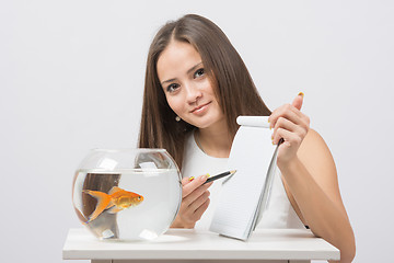 Image showing Girl shows a pen in a notebook record gold fish in the aquarium