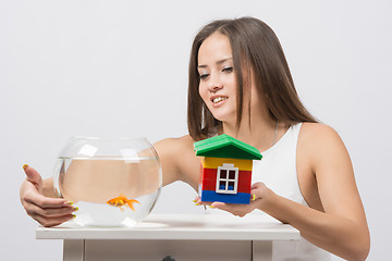 Image showing She knocks on the wall of the aquarium with goldfish and the other hand holding a toy house