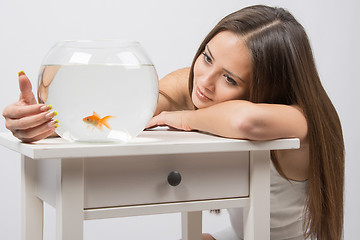 Image showing The girl looks at a small goldfish in a fishbowl