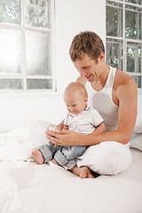 Image showing young father with his nine months old son on the bed at home