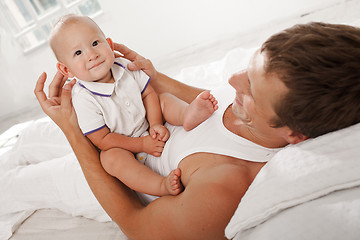 Image showing young father with his nine months old son on the bed at home