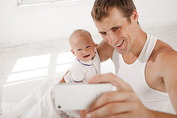 Image showing young father with his nine months old son on the bed at home