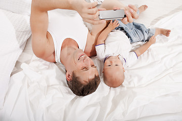 Image showing young father with his nine months old son on the bed at home