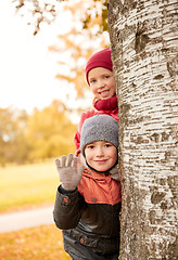 Image showing happy children hiding behind tree and waving hand