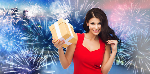 Image showing happy woman in red dress with gift over firework