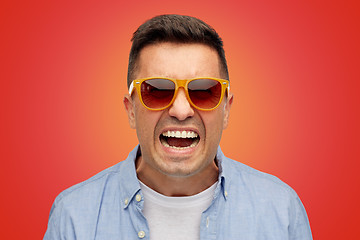 Image showing face of angry man in shirt and sunglasses over red