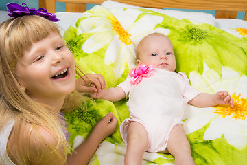 Image showing Five-year girl joyfully laughs while holding the handle of a newborn baby