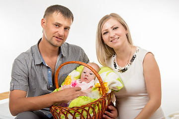Image showing Mom and dad sit on the bed and holding a two-month baby girl in a basket