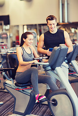 Image showing happy woman with trainer on exercise bike in gym