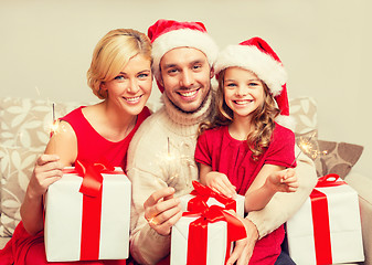 Image showing smiling family holding gift boxes and sparkles