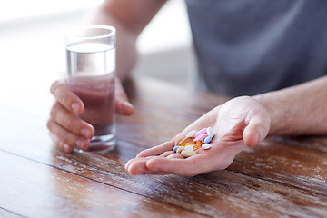 Image showing close up of male hands holding pills and water