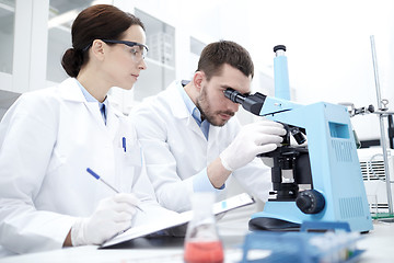 Image showing scientists with clipboard and microscope in lab