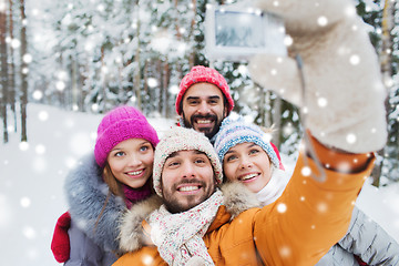Image showing smiling friends with camera in winter forest