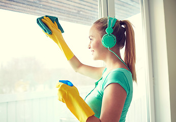 Image showing happy woman with headphones cleaning window