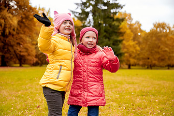 Image showing two happy little girls waving hand in autumn park