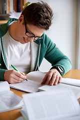 Image showing happy student boy writing to notebook in library