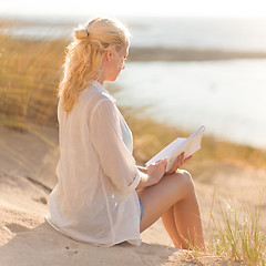 Image showing Woman enjoys reading on beautiful sandy beach.