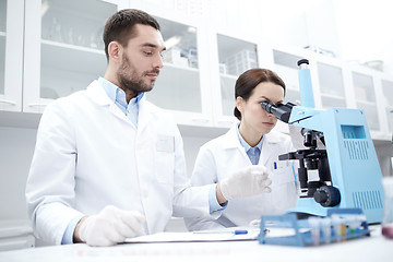 Image showing scientists with clipboard and microscope in lab