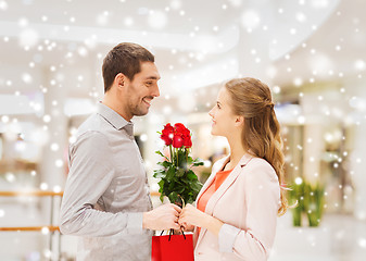 Image showing man giving woman red roses and present in mall