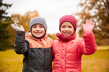 Image showing happy girl and boy waving hands in autumn park