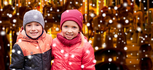 Image showing little girl hugging boy over snow and carousel