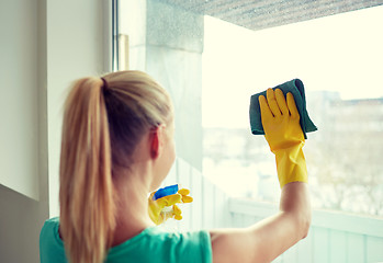 Image showing happy woman in gloves cleaning window with rag