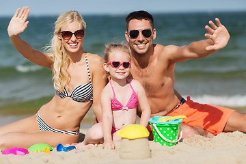 Image showing happy family with sand toys waving hands on beach