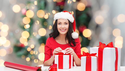 Image showing smiling woman in santa helper hat packing gifts