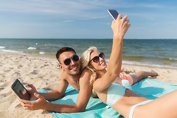 Image showing happy couple with modern gadgets lying on beach
