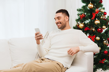 Image showing smiling man with smartphone at home for christmas